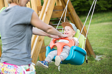 Image showing Mother pushing her infant baby boy child on a swing on playground outdoors.