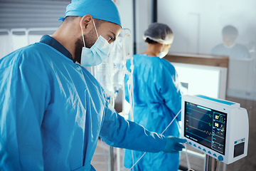 Image showing Doctor, hospital and medical machine with monitor screen during surgery for dialysis, healthcare and analysis in a room with a face mask and scrubs. Surgeon man pressing button on cardiology device