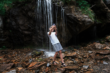 Image showing Boy tourist taking selfie photos with a smartphone at the waterfalls