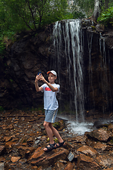 Image showing Boy tourist taking selfie photos with a smartphone at the waterfalls