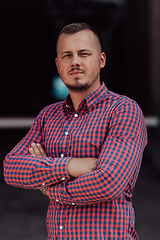 Image showing A successful young businessman in a shirt, with crossed arms, poses outdoors, confident expression on his face.