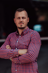 Image showing A successful young businessman in a shirt, with crossed arms, poses outdoors, confident expression on his face.