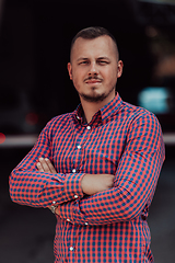 Image showing A successful young businessman in a shirt, with crossed arms, poses outdoors, confident expression on his face.