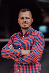 Image showing A successful young businessman in a shirt, with crossed arms, poses outdoors, confident expression on his face.