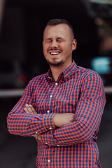 Image showing A successful young businessman in a shirt, with crossed arms, poses outdoors, confident expression on his face.