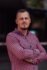 Image showing A successful young businessman in a shirt, with crossed arms, poses outdoors, confident expression on his face.