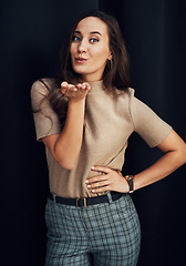 Image showing Fashion, beauty and woman blowing a kiss in studio on a dark background for love, romance or dating. Hand, portrait and smile with a happy young female standing indoors against a black wall alone