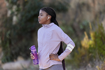 Image showing Fitness, running and black woman with water bottle in nature for wellness, minerals and healthy lifestyle. Exercise, sports and girl with earphones rest, breathe and relax after marathon training