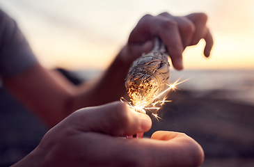 Image showing Hand, flame and sage burning at the beach for a spiritual ritual and meditation practice. Herb, finger and lighter with a plant being burned for zen meditative, mental health and chakra ceremony