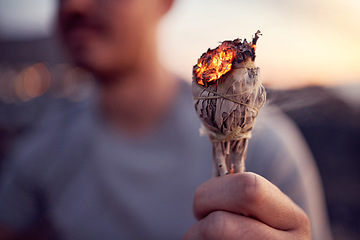 Image showing Man, hand and burning sage for a spiritual meditation on the beach at sunset for health and wellness. Smudge, burn herb and alternative healing ceremony to cleanse chakra in a meditating cleansing
