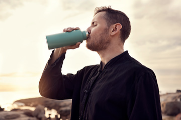 Image showing Drinking water, fitness and nature with a sports man or running taking a break on the beach during exercise. Training, sunset and health with a male athlete staying hydrated during a cardio workout