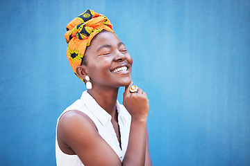 Image showing Fashion, style and trendy african woman on a blue wall or background with a headwrap. African american headwear, trend and beauty with a female fashion stylist in contemporary apparel and jewelry