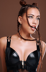 Image showing Fashion, edgy and sexy girl thinking with seductive bite and attractive black eyeliner makeup. Aesthetic, trendy and sensual black woman with cool leather clothing on brown studio background.