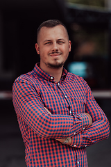 Image showing A successful young businessman in a shirt, with crossed arms, poses outdoors, confident expression on his face.