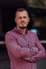 Image showing A successful young businessman in a shirt, with crossed arms, poses outdoors, confident expression on his face.