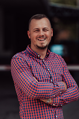 Image showing A successful young businessman in a shirt, with crossed arms, poses outdoors, confident expression on his face.