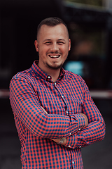 Image showing A successful young businessman in a shirt, with crossed arms, poses outdoors, confident expression on his face.