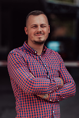 Image showing A successful young businessman in a shirt, with crossed arms, poses outdoors, confident expression on his face.