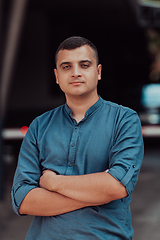 Image showing A successful young businessman in a shirt, with crossed arms, poses outdoors, confident expression on his face.