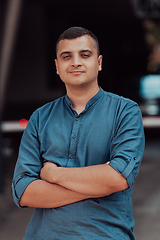 Image showing A successful young businessman in a shirt, with crossed arms, poses outdoors, confident expression on his face.