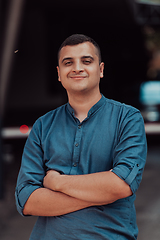 Image showing A successful young businessman in a shirt, with crossed arms, poses outdoors, confident expression on his face.