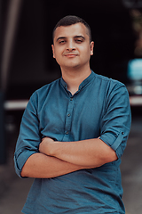 Image showing A successful young businessman in a shirt, with crossed arms, poses outdoors, confident expression on his face.