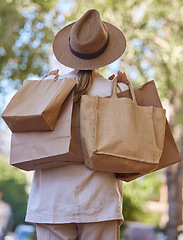 Image showing Sun, trees and woman with bags from shopping from back walking in park on holiday. Summer, nature and travel, girl with shopping bag from luxury designer boutique buying gifts on vacation garden path