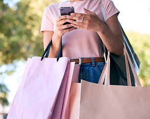Image showing Hands, phone and shopping bags with a woman customer outdoor in a park during summer for consumerism. Ecommerce, online shopping and retail with a female consumer using the internet to search a sale