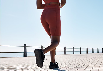 Image showing Black woman, legs and running for fitness at beach sidewalk, energy and strong summer body. Runner, healthy female and sports wellness at ocean for marathon, cardio exercise and workout on blue sky