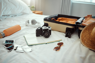 Image showing Hotel, travel and bedroom with a suitcase, camera and pictures on bed on holiday, vacation or trip. Hospitality, motel luggage and room with hat, sunglasses and notebook, headphones and water bottle.