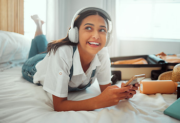 Image showing Music, relax and phone with woman and suitcase for travel, summer break and holiday. Technology, headphones and packing clothes with girl on bed of hotel or airbnb for vacation, schedule and booking