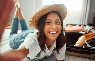 Image showing Face, travel selfie and woman packing suitcase getting ready for vacation or holiday. Portrait, relax and happy female taking pictures in hat while loading luggage on bed in preparation for trip.