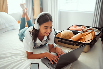 Image showing Computer travel and woman packing for a vacation with headphones typing a holiday blog. Adventure, planning and female happy on a hotel room bed with a luggage, suitcase and bag ready for a journey