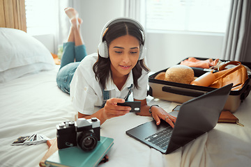 Image showing Travel, woman and bedroom booking on laptop with credit card for holiday planning with music streaming. Vacation preparation and online payment of girl with headphones on bed with luggage in home.