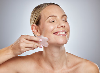 Image showing Gua sha, skincare and woman with face massage, self care product and spa wellness against a grey studio background. Beauty facial, smile and model massaging skin for anti aging and natural glow