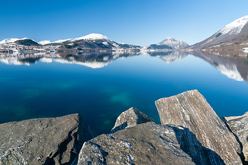 Image showing snow-covered mountain range reflected in blue sea with rocks in 