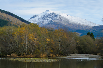 Image showing autumn-colored trees by the river and high snow-covered mountain