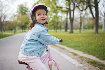 Image showing Kids, bike and learning to ride with a girl in the park on her bicycle while wearing a helmet for safety outdoor. Summer, cycling and children with a happy female child training to cycle in a garden