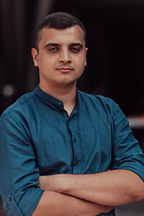 Image showing A successful young businessman in a shirt, with crossed arms, poses outdoors, confident expression on his face.