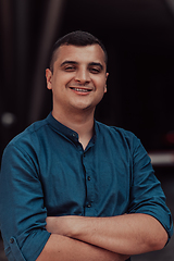 Image showing A successful young businessman in a shirt, with crossed arms, poses outdoors, confident expression on his face.