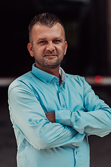 Image showing A successful young businessman in a shirt, with crossed arms, poses outdoors, confident expression on his face.