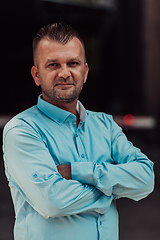 Image showing A successful young businessman in a shirt, with crossed arms, poses outdoors, confident expression on his face.