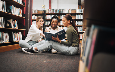 Image showing University, students and women in library with book working on, researching and looking up information for group research project. College, student diversity and friends working on homework together