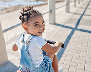 Image showing Bike, girl and smile for beach, holiday and outdoor to relax, summer and waterfront. Portrait, cycling and female child enjoy seaside vacation, happy and bicycle for wellness, health and promenade.