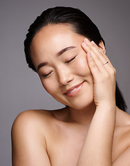 Image showing Face, beauty and skincare with a model asian woman touching her skin in studio on a gray background. Relax, wellness or cosmetics with an attractive young female posing for a luxury skin care product