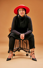 Image showing Fashion, beauty and senior woman on chair in studio on brown background with stylish, cool and trendy outfit. Creative art, style and Muslim female model with designer clothes and luxury accessories