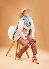 Image showing Muslim woman, fashion scarf or chair in studio background in Dubai stylish, trendy hats or cool arabic clothes. Happy smile, laughing or mature Islamic model on furniture seat with hijab fabric scarf