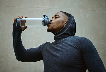 Image showing Black man, running and drinking water for health and wellness during exercise, workout and cardio training with hood. Face of athlete male with sports bottle for hydration during urban fitness run