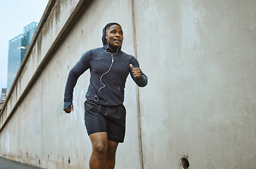 Image showing Black man, fitness and running in the city with earphones listening to music during cardio workout. Active African American man runner enjoying audio track, healthy exercise or training in urban town