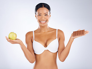 Image showing Black woman, health and food choice for diet, nutrition or skincare vitamins against a grey studio background. Happy woman smiling in bra holding apple and chocolate in weight loss or body care plan